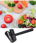 Handheld spiral vegetable slicer, black plastic with metal blade, shown beside fresh salad vegetables