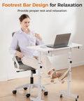 Compact Adjustable Standing Desk On Wheels For Home Office with footrest bar, white 32 inch workstation, woman seated with laptop.