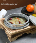 Dolsot style granite stone bowl with lid, 14 cm, on wooden holder, filled with soup, showcasing heat-retaining features.
