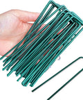 Hand holding Heavy Duty Garden Stakes And Ground Anchors Set 10 Pack Galvanized U Hooks for lawn beds and landscape weed barrier.