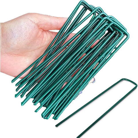 Hand holding Heavy Duty Garden Stakes And Ground Anchors Set 10 Pack Galvanized U Hooks for lawn beds and landscape weed barrier.