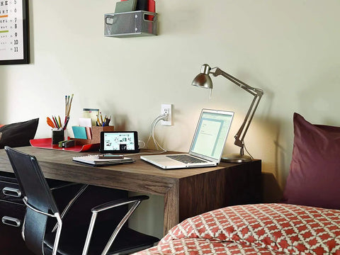Smart In-Wall USB Charger With 15A Tamper-Resistant Outlet installed near a desk with a laptop and lamp.
