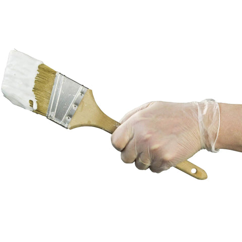 Hand holding a paintbrush covered in white paint while wearing Heavy Duty Clear Vinyl Industrial Gloves Case Of 1000 Units 3 Mil Thick Build.