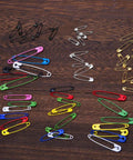 Kickass Assorted Steel Safety Pins Bulk Kit For Sewing Tailoring And Crafting in various colors on wooden background.