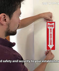 Person installing Fire Extinguisher Signs Stickers 12 Pack 4x12 Inch Premium Self Adhesive Vinyl Decals Laminated For Ultimate UV Weather Scratch Water Fade Resistance Indoor Outdoor Easy To View Location Indicator For Fire Extinguishers on wall
