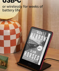 Kindle Paperwhite Signature Edition 7 Inch E Reader With 32GB Storage Featuring Auto Adjusting Front Light Wireless Charging And Sweet Long Battery Life In Sleek Metallic Black charging via USB-C on a stylish wooden table.