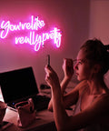 Pink Led Neon Sign Youre Like Really Pretty With Safe Acrylic Backing illuminating a woman's desk in a bedroom setting.