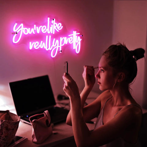 Pink Led Neon Sign Youre Like Really Pretty With Safe Acrylic Backing illuminating a woman's desk in a bedroom setting.