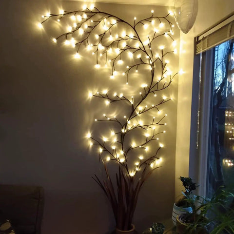 Lit Up Willow Vine Lights For Indoor Or Outdoor Decor With Plug In Power Flexible Faux Plant glowing against wall near window