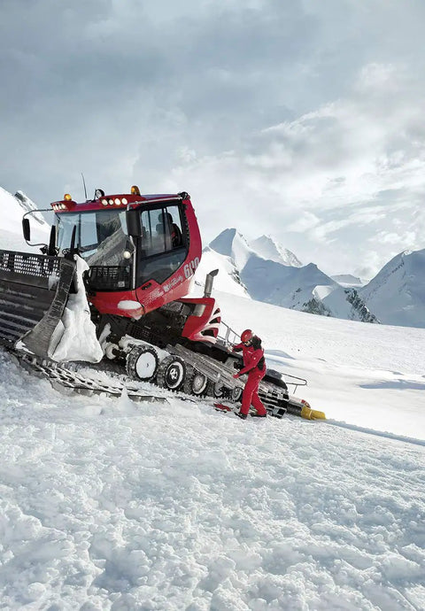 Snow plow clearing snow on mountain slope with operator adjusting equipment, focus on machinery and snowy landscape.