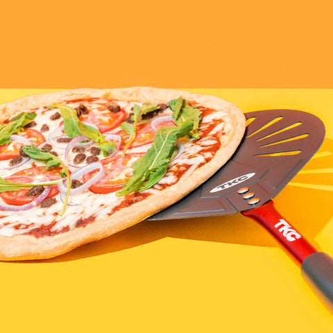 Pizza peel, 9-inch perforated aluminum with red handle, TKC branding, angled view under a veggie pizza.