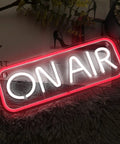 "ON AIR" neon sign in red frame, resting on a textured surface with plants; not the Happy Birthday Neon Sign Wall Decor