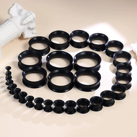 Dope Black Silicone Ear Gauges Set With 15 Pairs And 24 Pieces Stretching Kit For Ear Tunnels From 2G To 25mm displayed on table