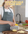 Front view: person in a gray apron uses a yellow-handled crinkle cutter to slice a potato on a cutting board.