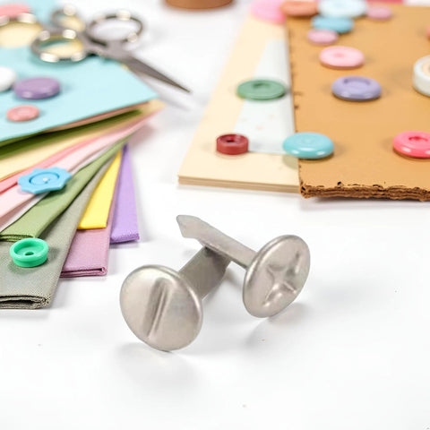 Top Tier 100 Pack 8mm Slotted Phillips Head Screw Brads In Sleek Silver on a crafting table with colorful paper, buttons, and scissors.