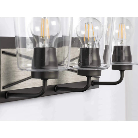 Close-up of three-light coastal bath vanity light with clear glass, rustic X-brace design, faux woodgrain backplate, graphite black finish