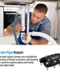 Under-sink view of a plumber installing a drain pipe repair clamp kit on white PVC pipe with a gray hose and black bolted clamp.