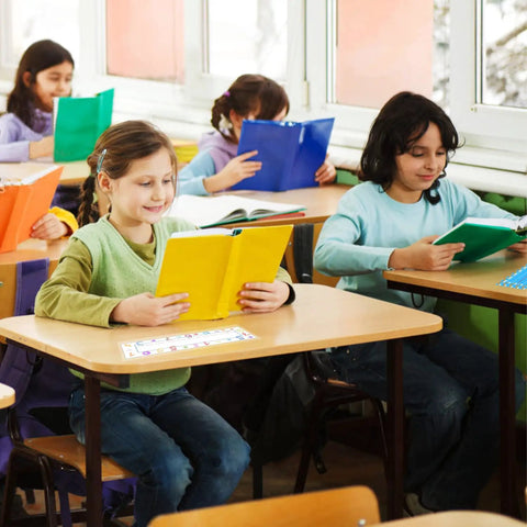 Children reading at desks, clear plastic desk nameplate pockets visible, enhancing classroom organization and personalization.