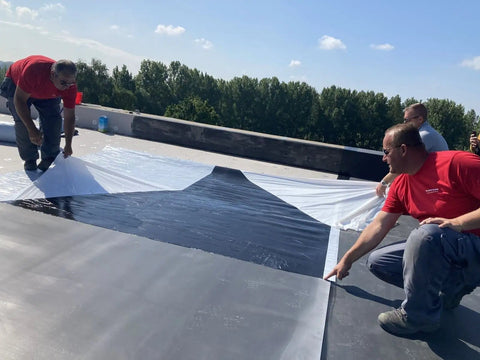 Two roofers laying down Heavy Duty 45 Mil EPDM Roofing Membrane 10 Feet By 200 Feet Roll for flat roofs.