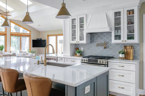 Modern kitchen with white cabinets, marble countertop, gas stove, and brass fixtures under natural light.