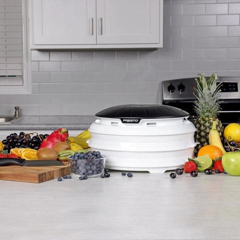 Electric Food Dehydrator With Four Stackable Trays And Top Mounted Fan, surrounded by fresh fruits and veggies on a kitchen counter.