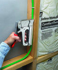 Pro Grade Heavy Duty T72 Wire And Cable Stapler securing green wire to wooden frame, ideal for telecommunications and data installations.