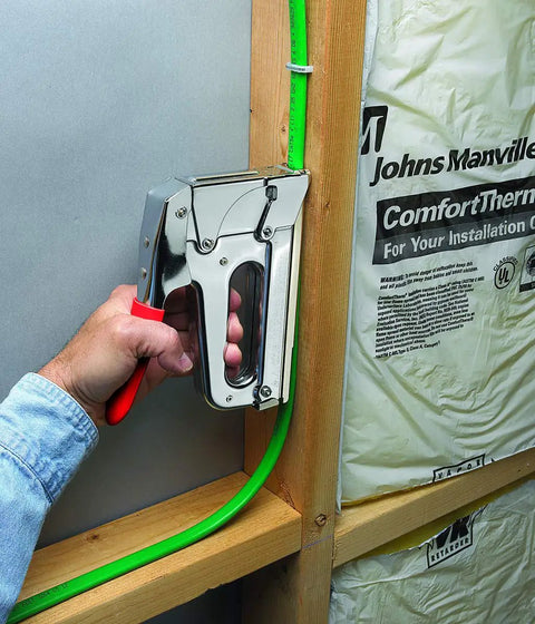 Pro Grade Heavy Duty T72 Wire And Cable Stapler securing green wire to wooden frame, ideal for telecommunications and data installations.
