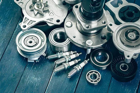 Assorted metal mechanical parts and spark plugs on a wooden surface, suitable for use with Industrial Strength Penetrating Grease Lubricant Aerosol 13 Oz with Extension Tube for Tight Areas Heavy Duty Long Lasting Lubrication Penetrates Metal Parts and Machinery.