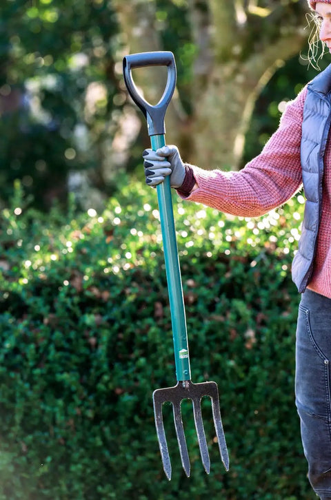 Person holding compact steel-handle border fork with a 6-inch shorter design, ergonomic grip, and durable tines for garden beds.