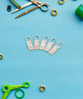 Top Shelf Universal Replacement Zipper Pull Heads 20 Piece Metal Kit on blue surface with scissors and various materials.