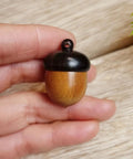 Hella Slick Screw Open Miniature Black Ebony Acorn Curios Set Of Two With Hidden Antique Bronze Pinecones For Super Dope Fall Harvest Woodland Decor, held in hand.