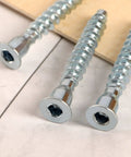 Close-up of 100 Pack M7x50mm Hex Socket Countersunk Self Tapping Screws for heavy-duty furniture cabinets, zinc plated.