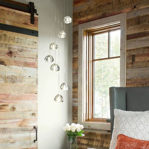 Modern LED Crystal Chandelier Pendant Lighting With Seven Lights In Chrome Finish hanging in a rustic room, next to a wooden sliding door and window.