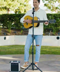 Musician using Heavy Duty Floor Microphone Stand With Boom Arm in outdoor setting, with guitar and amplifier nearby.