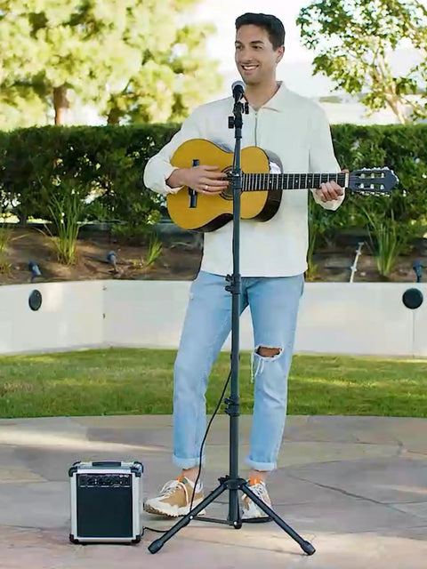 Musician using Heavy Duty Floor Microphone Stand With Boom Arm in outdoor setting, with guitar and amplifier nearby.