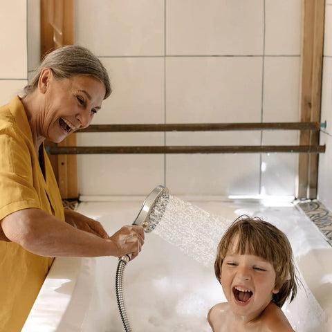 Smiling woman using Magnetic 2 In 1 Shower Head With Handheld Sprayer And On Off Water Saving Switch Eight Spray Hand Held Wand Flexible Anti Kink Hose Brushed Nickel Finish For Easy Docking And Strong Water Pressure to bathe a child in a tub.