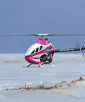 M2 V3 Sport BNF RC Helicopter For Adults With OFS3 Plus Flight Controller in flight over a snowy landscape, pink design.
