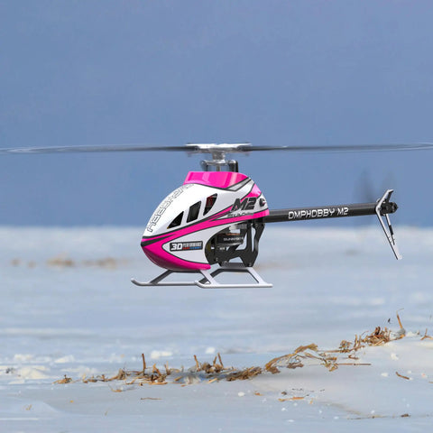 M2 V3 Sport BNF RC Helicopter For Adults With OFS3 Plus Flight Controller in flight over a snowy landscape, pink design.