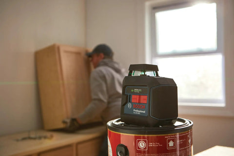 Green Beam Self Leveling 360 Degree Cross Line Laser in use, mounted on a paint can, with a person installing cabinetry.