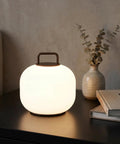 Cordless RGBW LED Table Lamp With Remote Control on bedside table, glowing with warm light, alongside books and vase.