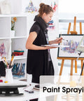 11 Inch Rotate Turntable For Cake Decorating And Painting With Smooth Ball Bearing Spin And 360 Degree Rotation Black Lightweight Display Stand For Spinning Spraying Decorating And Sculpting Projects By Kootek shown on an art studio table with a woman painting in the background.