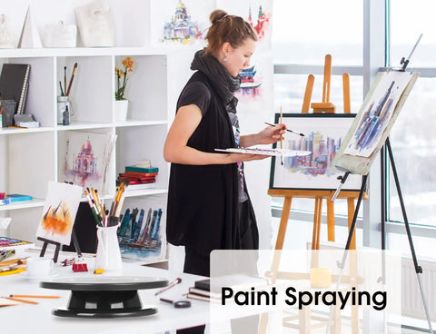 11 Inch Rotate Turntable For Cake Decorating And Painting With Smooth Ball Bearing Spin And 360 Degree Rotation Black Lightweight Display Stand For Spinning Spraying Decorating And Sculpting Projects By Kootek shown on an art studio table with a woman painting in the background.