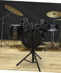 Adjustable Snare Drum Stand With Practice Pad Mount Alloy Build designed for stability with a sleek black finish, set near a drum kit.