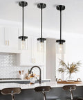 Lit Modern Clear Glass Pendant Lights 3 Pack Adjustable Hanging Lighting For Kitchen Island Hallway Porch Bedroom 60W Equivalent Height Adjustable Cord Sleek Minimalist Ceiling Fixture installed over a kitchen island with white cabinetry and black bar stools.