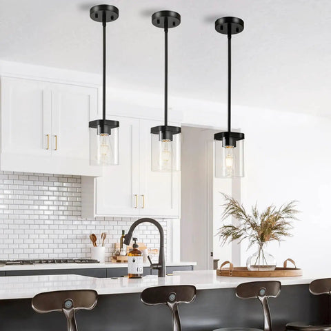 Lit Modern Clear Glass Pendant Lights 3 Pack Adjustable Hanging Lighting For Kitchen Island Hallway Porch Bedroom 60W Equivalent Height Adjustable Cord Sleek Minimalist Ceiling Fixture installed over a kitchen island with white cabinetry and black bar stools.
