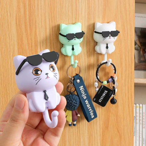 Three Cool Cat Key Holder With Sunglasses No Drill Adhesive Hooks on wood wall, holding keys and small accessories, hand holding one hook.