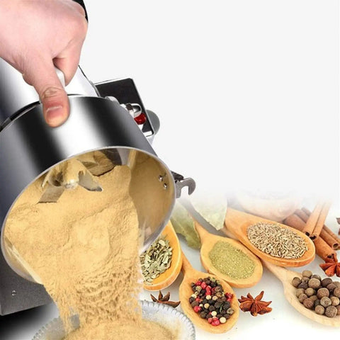 Beast Mode High Speed 2500G Stainless Steel Grain Grinder Mills pouring spice powder, surrounded by herbs and spices.