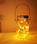 Lit Solar Mason Jar Lights 4 Pack With 30 LEDs Starry Fairy String Hanging Jar Lights glowing on a table