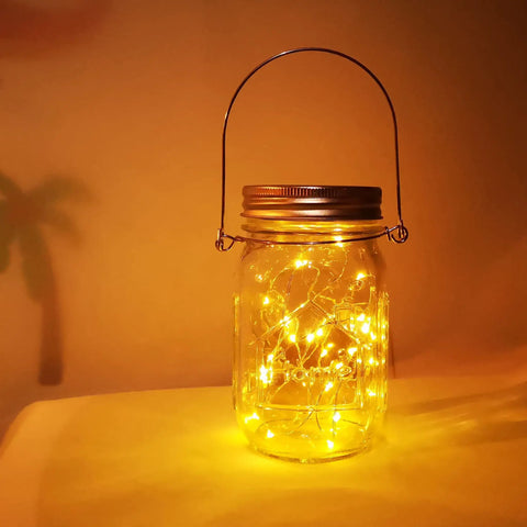 Lit Solar Mason Jar Lights 4 Pack With 30 LEDs Starry Fairy String Hanging Jar Lights glowing on a table