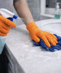 Person using Built Tough 10 Mil Nitrile Gloves With Rock Solid Diamond Grip to clean a countertop with spray and cloth.